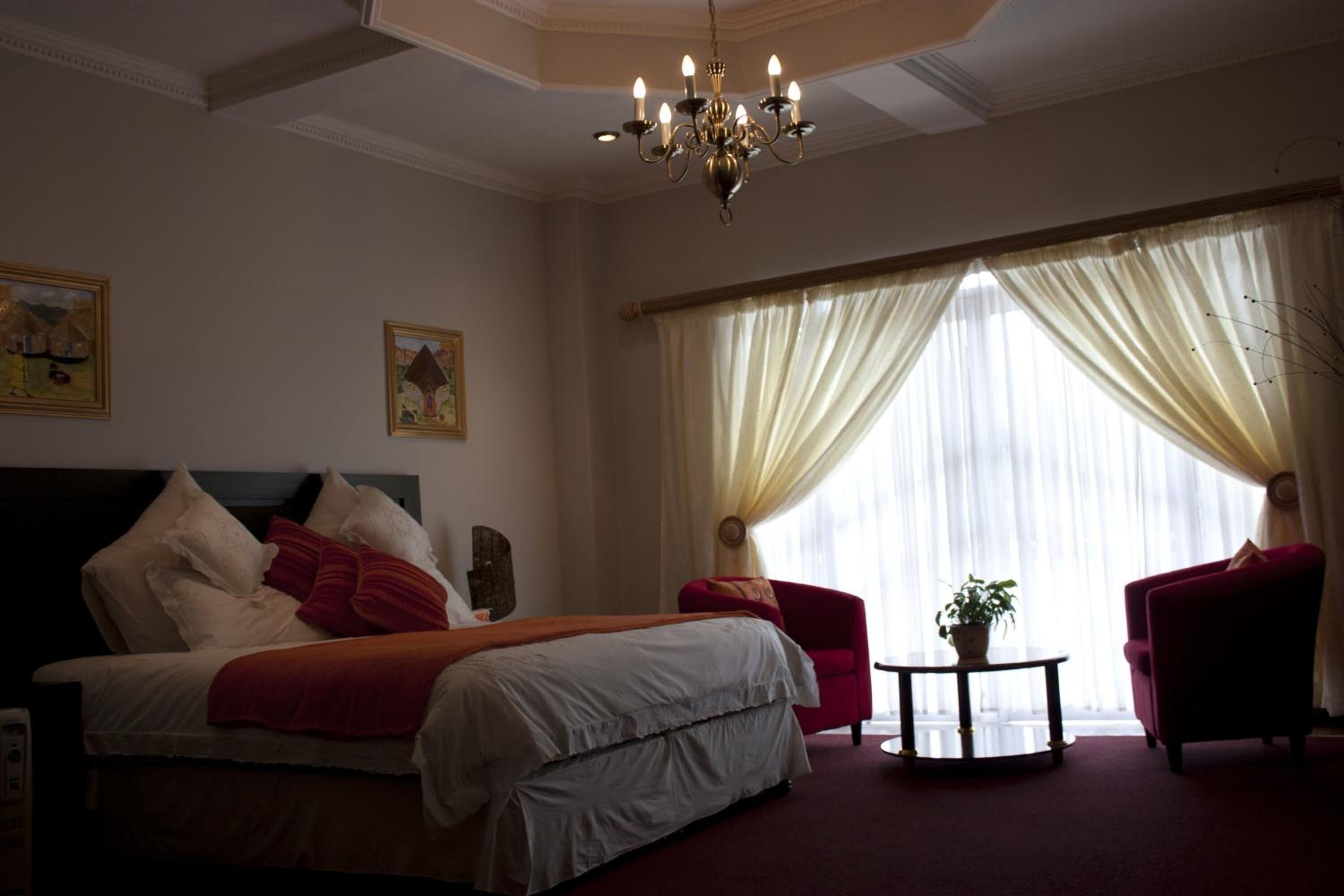 Ein Hotelzimmer mit einem großen Bett, zwei Sesseln, einem kleinen Tisch mit einer Pflanze und einer Kandelaber.