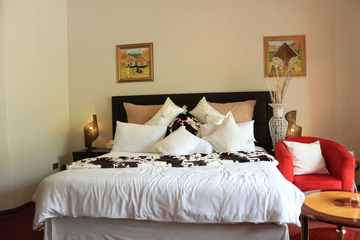 A neatly made bed with a white and black patterned bedspread, a red armchair, and two wall-mounted lamps.