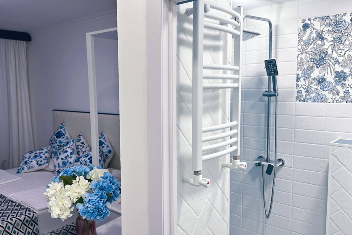 Une chambre d’hôtel comprenant un lit, une table de chevet, un vase avec des fleurs et un espace douche avec un porte-serviettes.