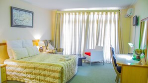 A hotel room with a bed, desk, chair, and a large window with curtains. - Mountain View Hotel (Hlotse)