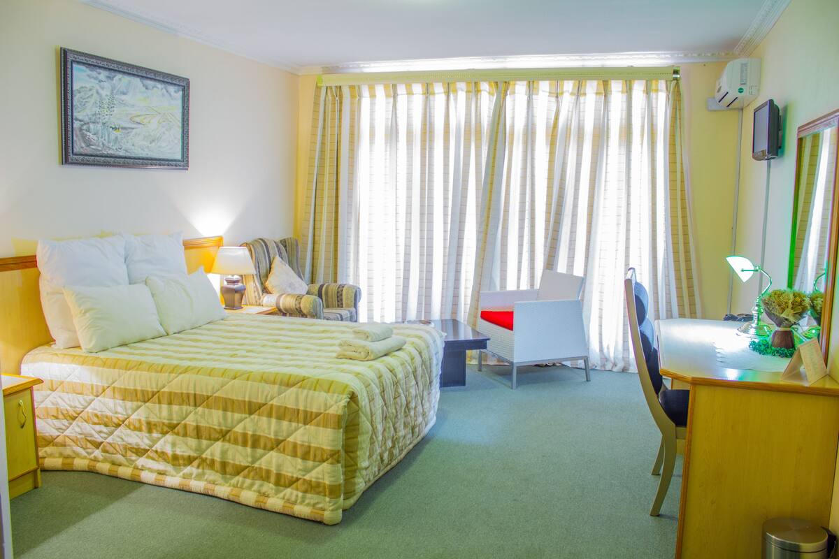 A hotel room with a bed, desk, chair, and a large window with curtains.