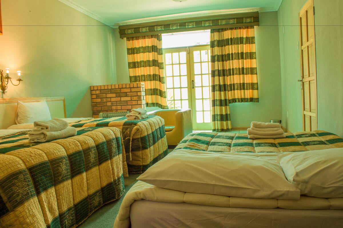 A hotel room with two beds, a brick fireplace, a yellow armchair, and a window with striped curtains.