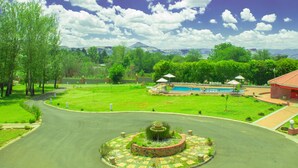 A landscaped area with a pool, a fountain, and a building with a red roof. - Mountain View Hotel (Hlotse)