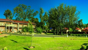 A large, multi-story building with a red roof and brick facade, surrounded by well-maintained lawns and trees. - Mountain View Hotel (Hlotse)