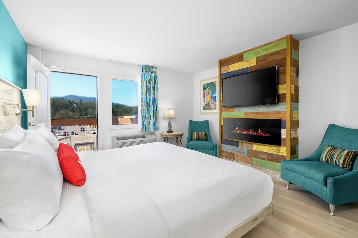 A hotel room with a large bed, two armchairs, a TV, a fireplace, and a view of the outdoors.