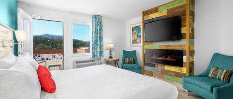 A hotel room with a large bed, two armchairs, a TV, a fireplace, and a view of the outdoors.