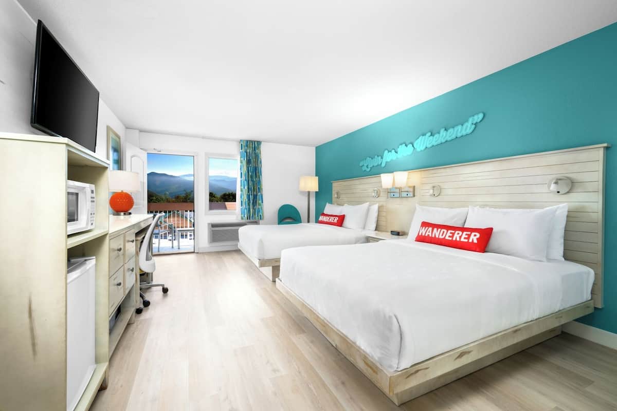 A hotel room with two beds, a TV, a desk with a lamp, and a view of mountains.