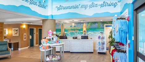 A hotel lobby with a beach-themed mural, a reception desk, and a merchandise display.