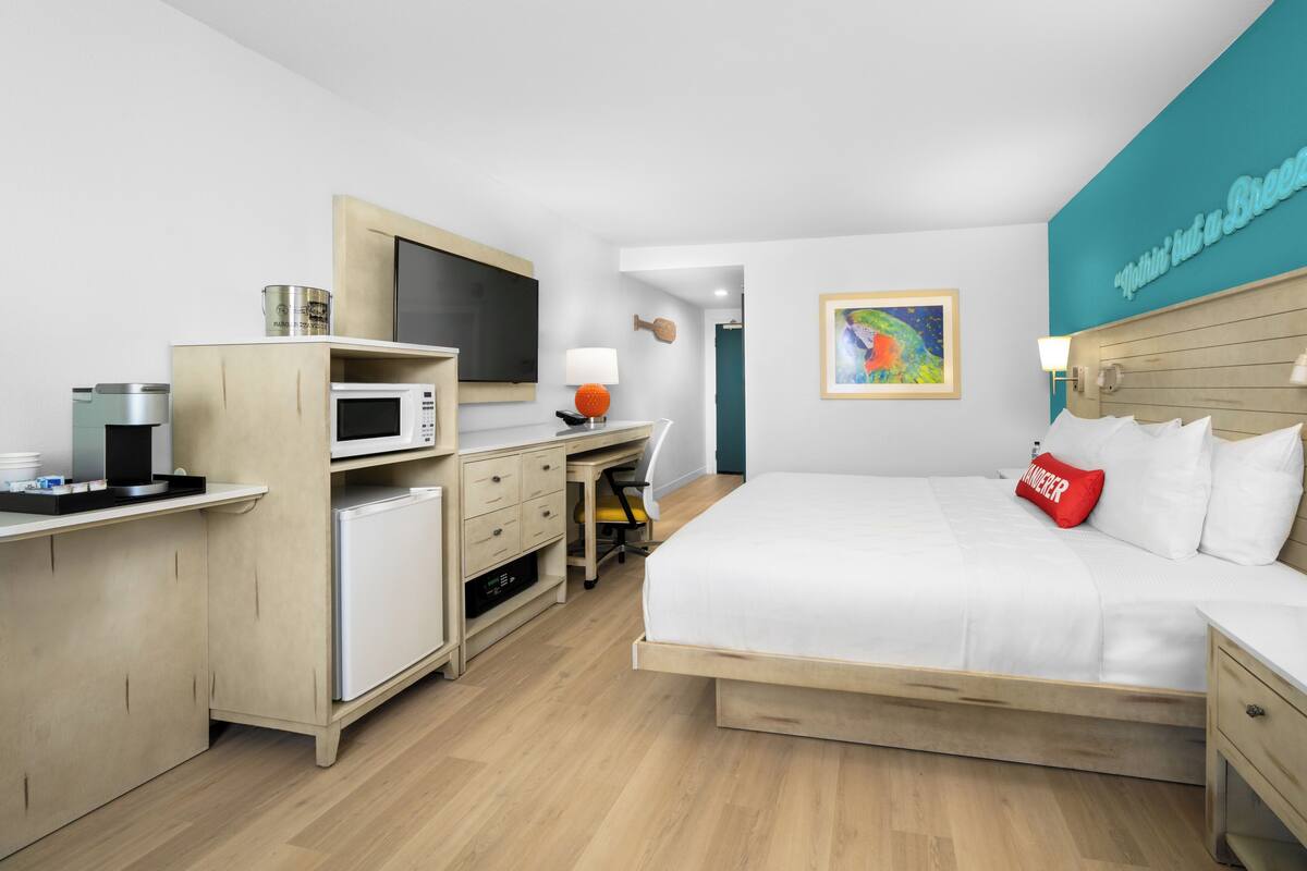 A hotel room with a bed, desk, microwave, and a painting on the wall.