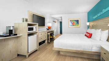 Habitación de hotel con cama, escritorio, microondas y un cuadro en la pared.