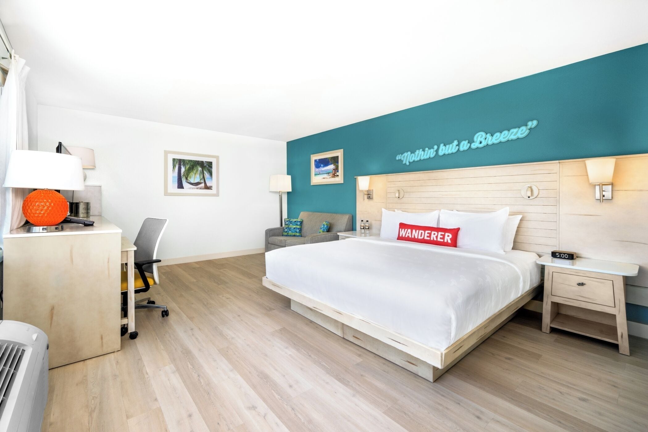 A hotel room with a bed, a desk, a chair, a nightstand, and a wall with a sign.