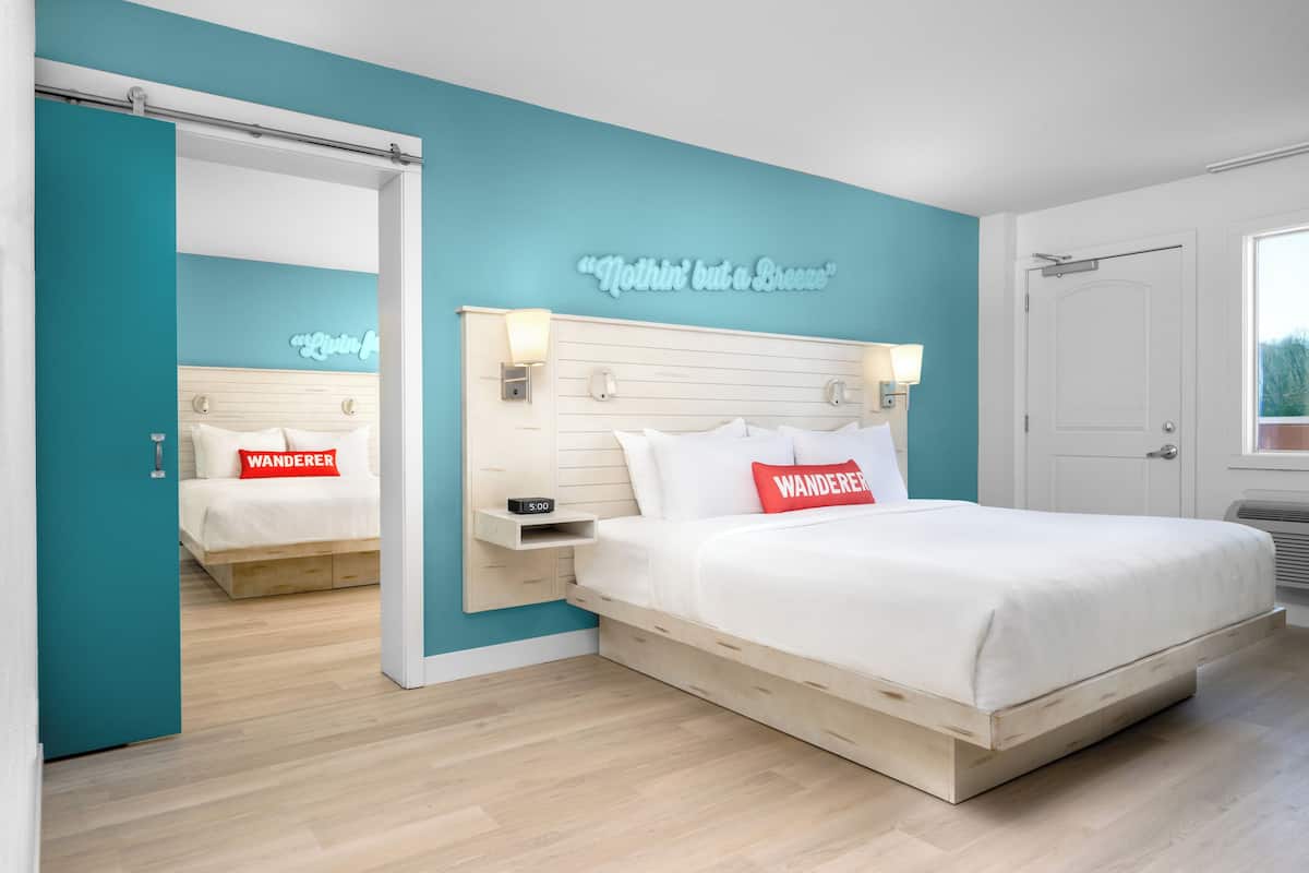 A modern bedroom with a teal accent wall, a wooden bed frame, and a mirror reflecting the room.