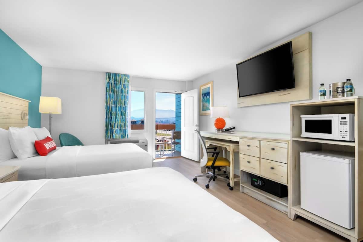 A hotel room with two beds, a desk with a computer, a TV, a microwave, and a mini-fridge.