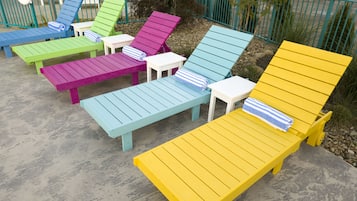 A row of colorful Adirondack chairs with matching cushions, arranged on a concrete patio.
