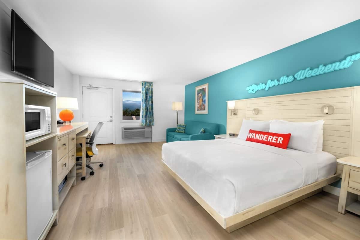 A modern hotel room with a bed, a desk, a TV, and a view of the outdoors.