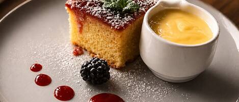 A dessert with a berry compote, a blackberry, and a small bowl of sauce on a plate.