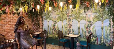 Un restaurant décoré d’une fresque représentant des plantes tropicales, d’une statue de femme et d’un sol recouvert de carreaux à motifs.
