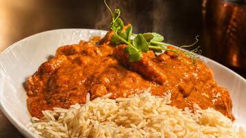A plate of chicken curry with rice and a sprig of herb.