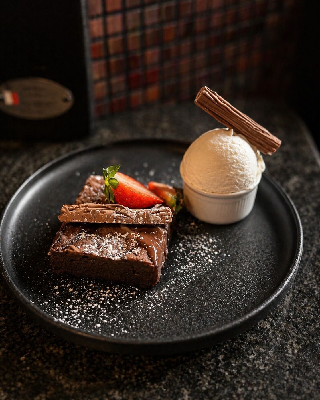 A dessert plate with brownies, strawberries, and a scoop of ice cream.