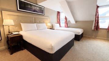Ein Hotelzimmer mit einem großen Bett, einem kleineren Bett, einem Nachttisch mit Lampe und einem gerahmten Bild an der Wand.