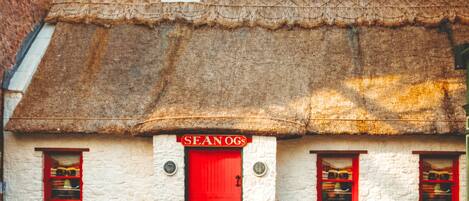 A traditional building with a thatched roof, a red door, and two barrels.