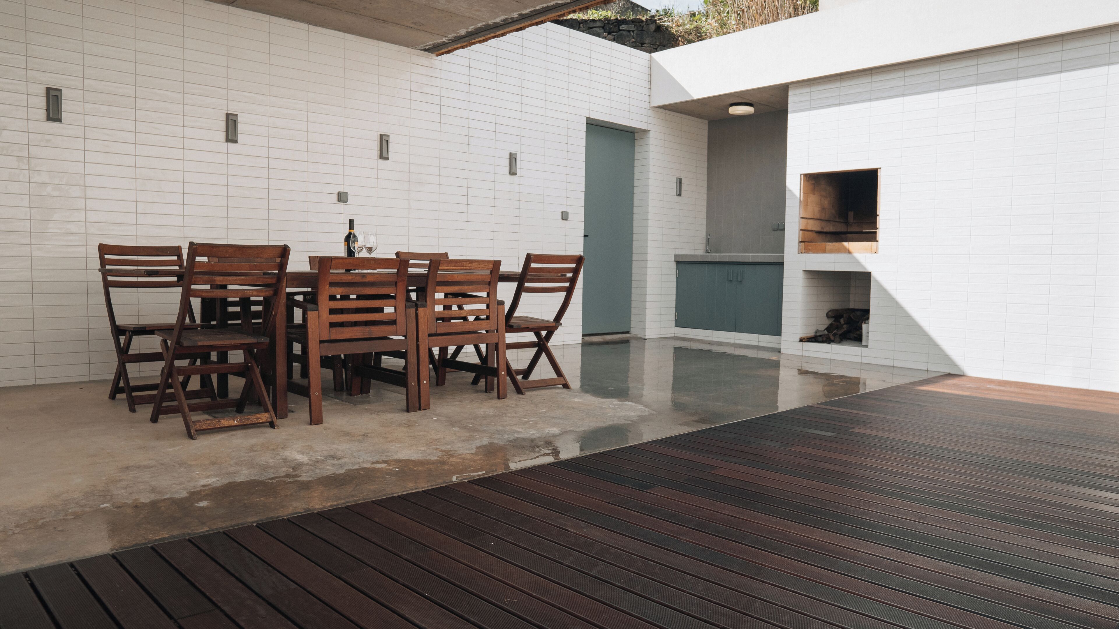 A modern outdoor dining area with a wooden table and chairs, a tiled wall, and a concrete floor.