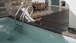 Ein Swimmingpool mit Holzterrasse, einer Steinmauer und einem Essbereich mit Stühlen und Tisch.