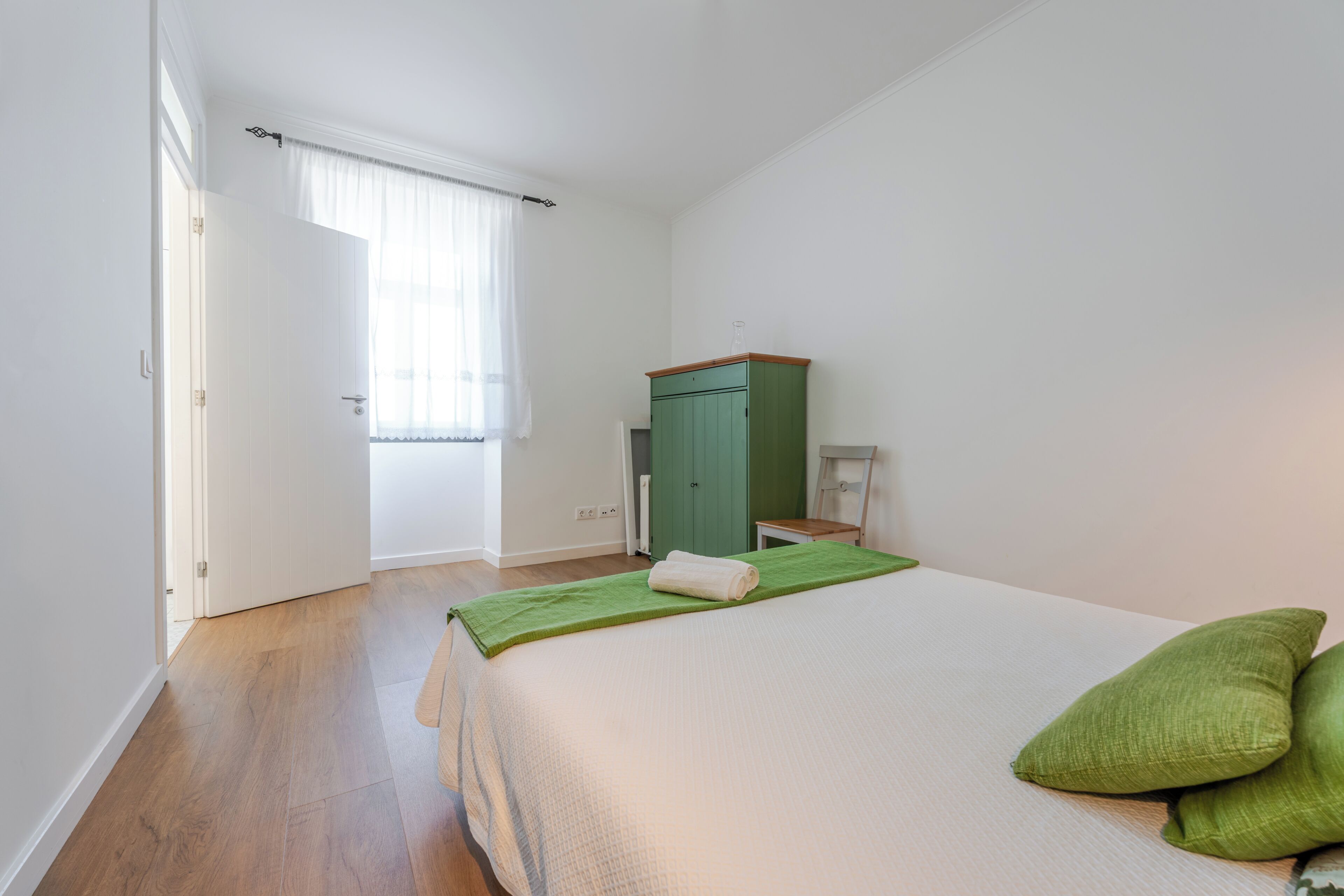 A bedroom with a bed, a green cabinet, and a window with curtains.