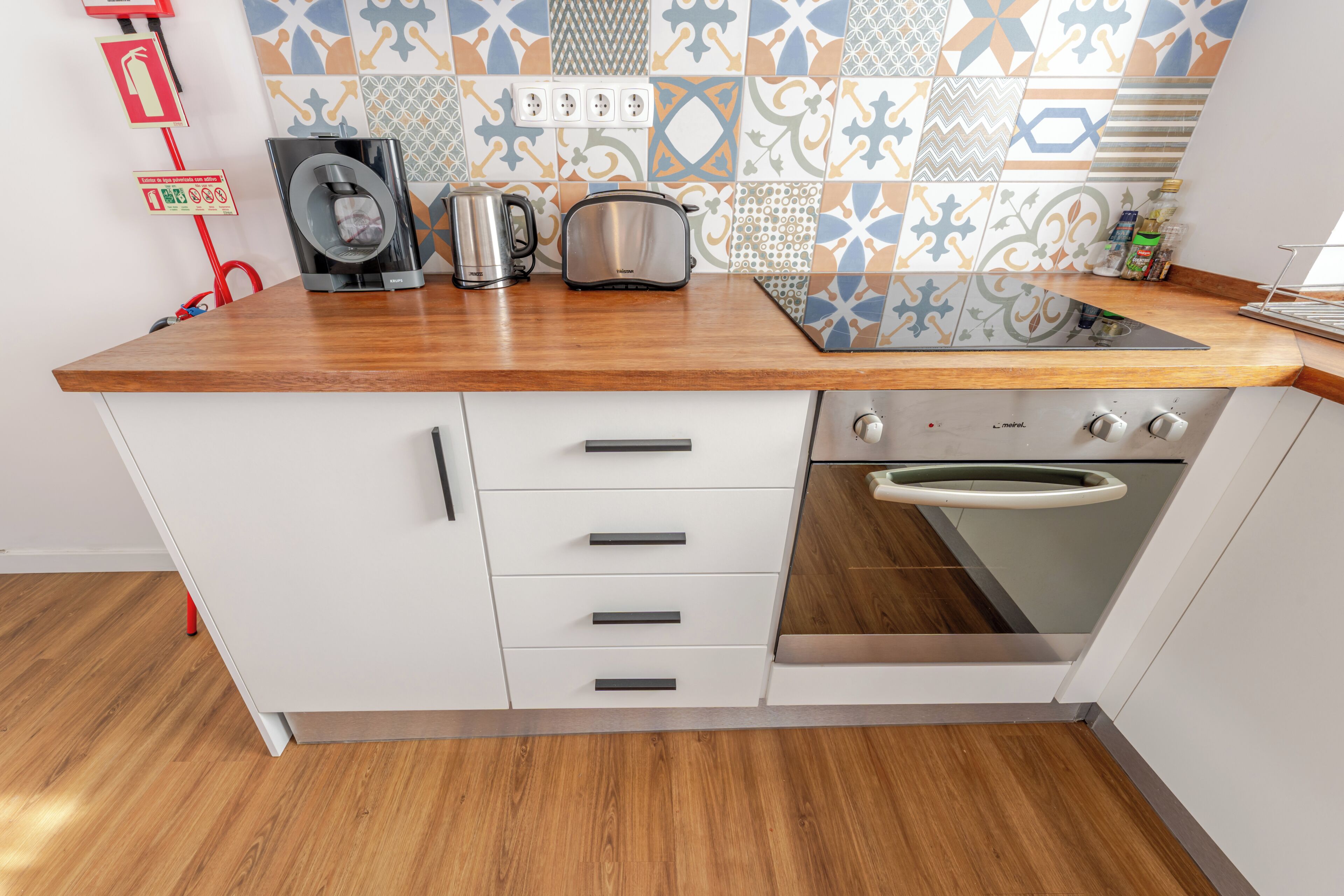 A kitchen with a wooden countertop, stainless steel appliances, a built-in oven, and patterned backsplash tiles.