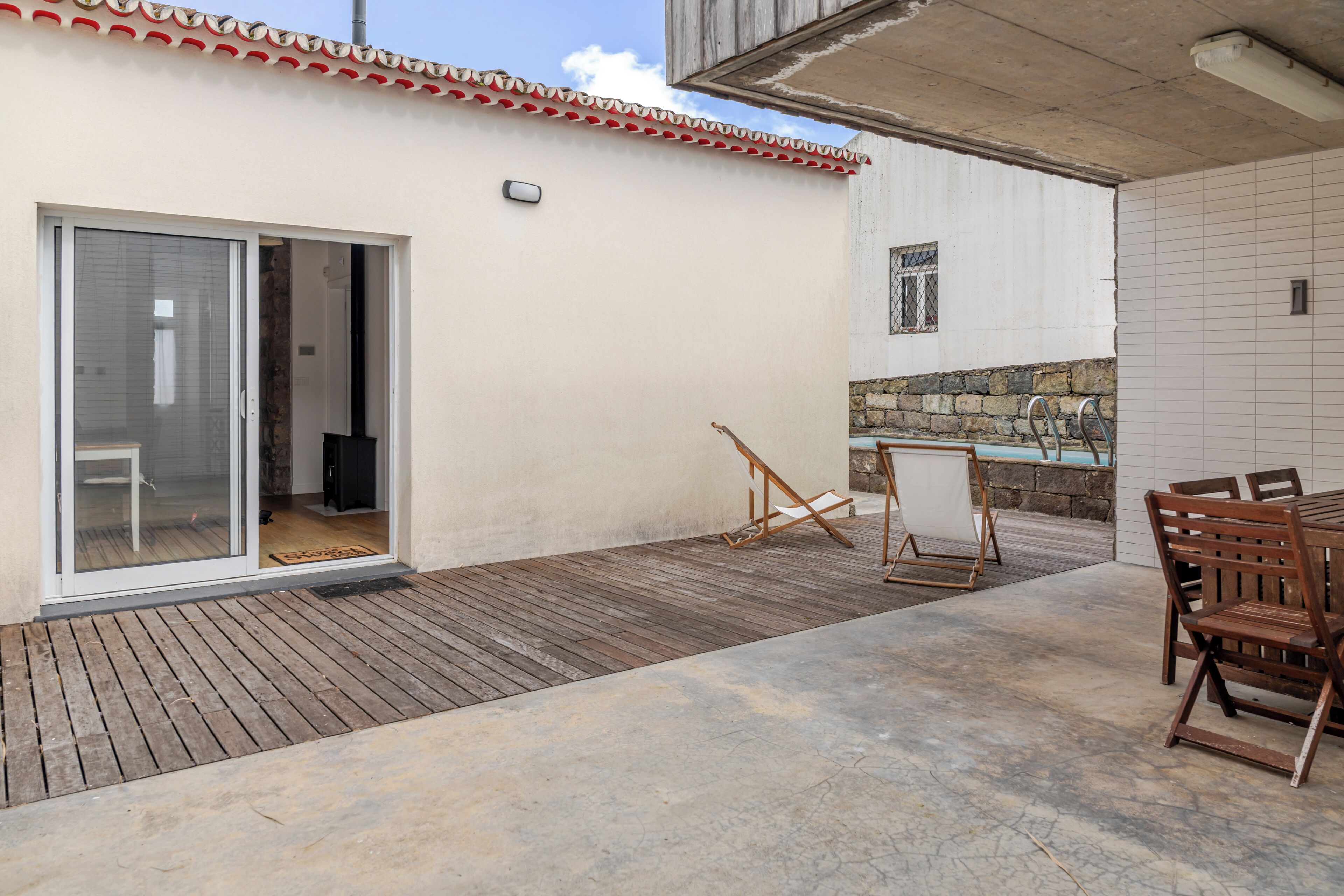 A patio with a wooden deck, a sliding glass door, a small table with chairs, and a stone wall.