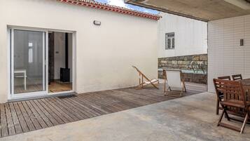 A patio with a wooden deck, a sliding glass door, a small table with chairs, and a stone wall.