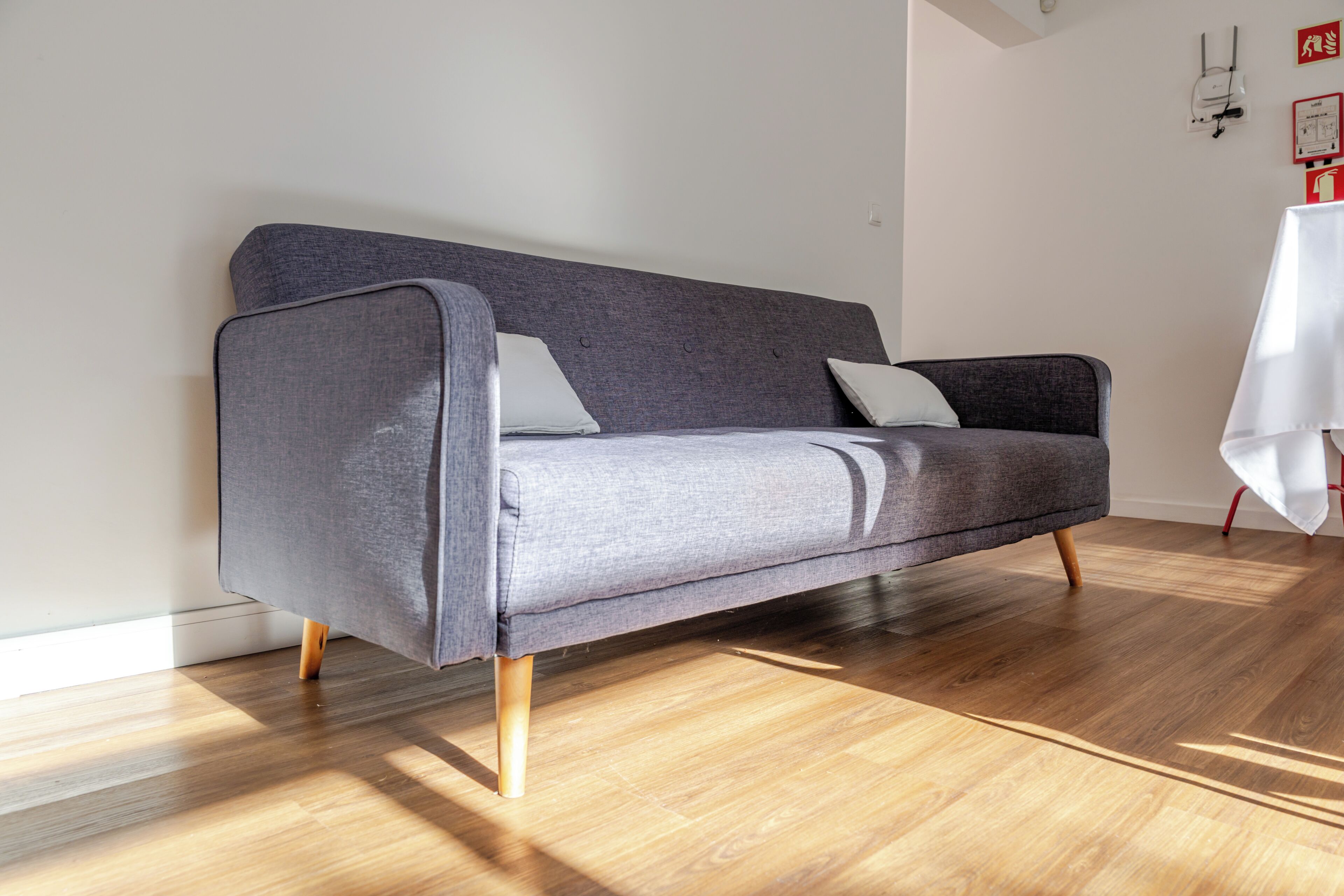 Un sofá gris con patas de madera en una habitación con suelo de madera y paredes blancas.