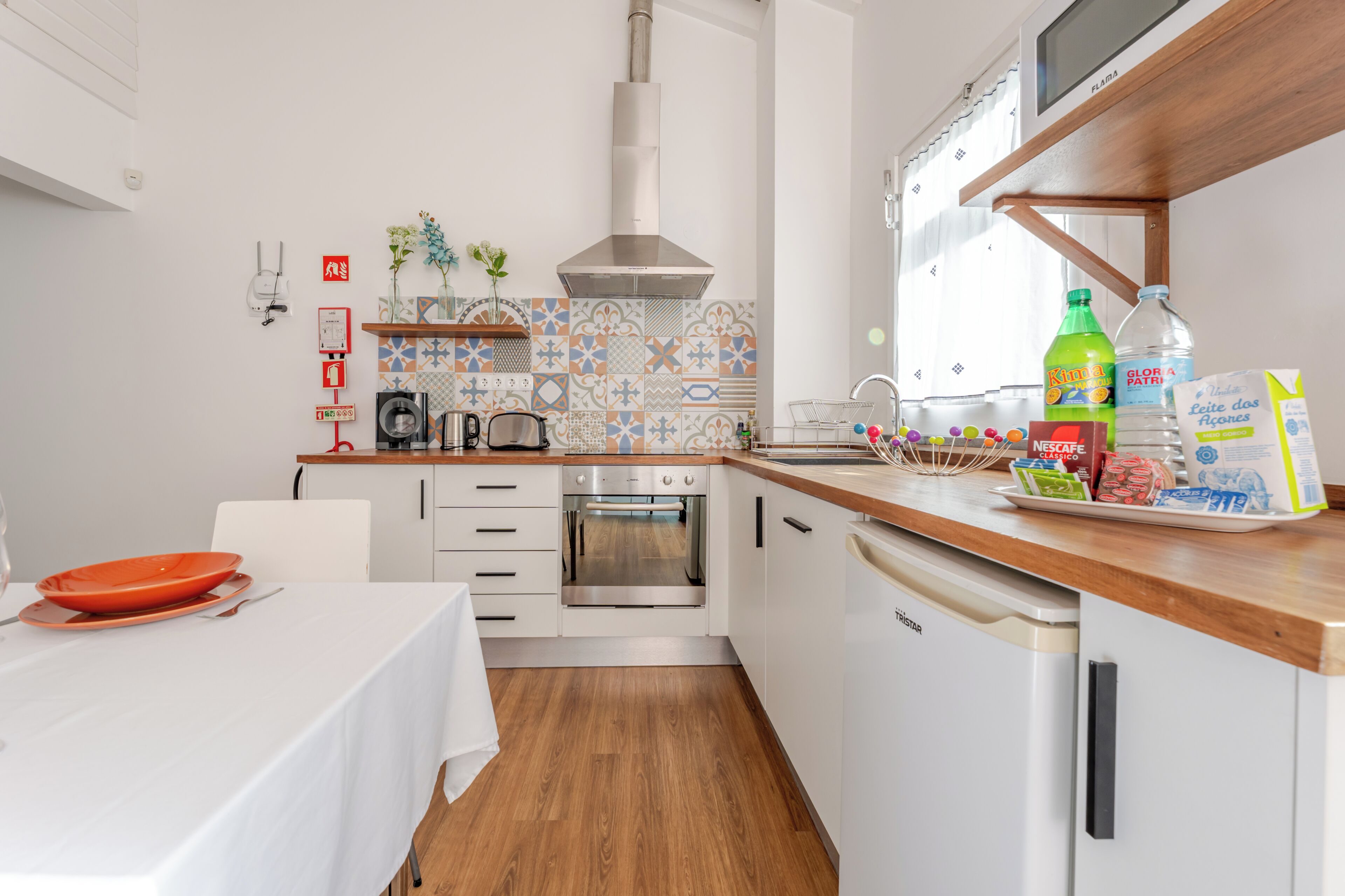 A modern kitchen with white cabinetry, a stainless steel oven, a wooden countertop, and a dining area with a table set for two.