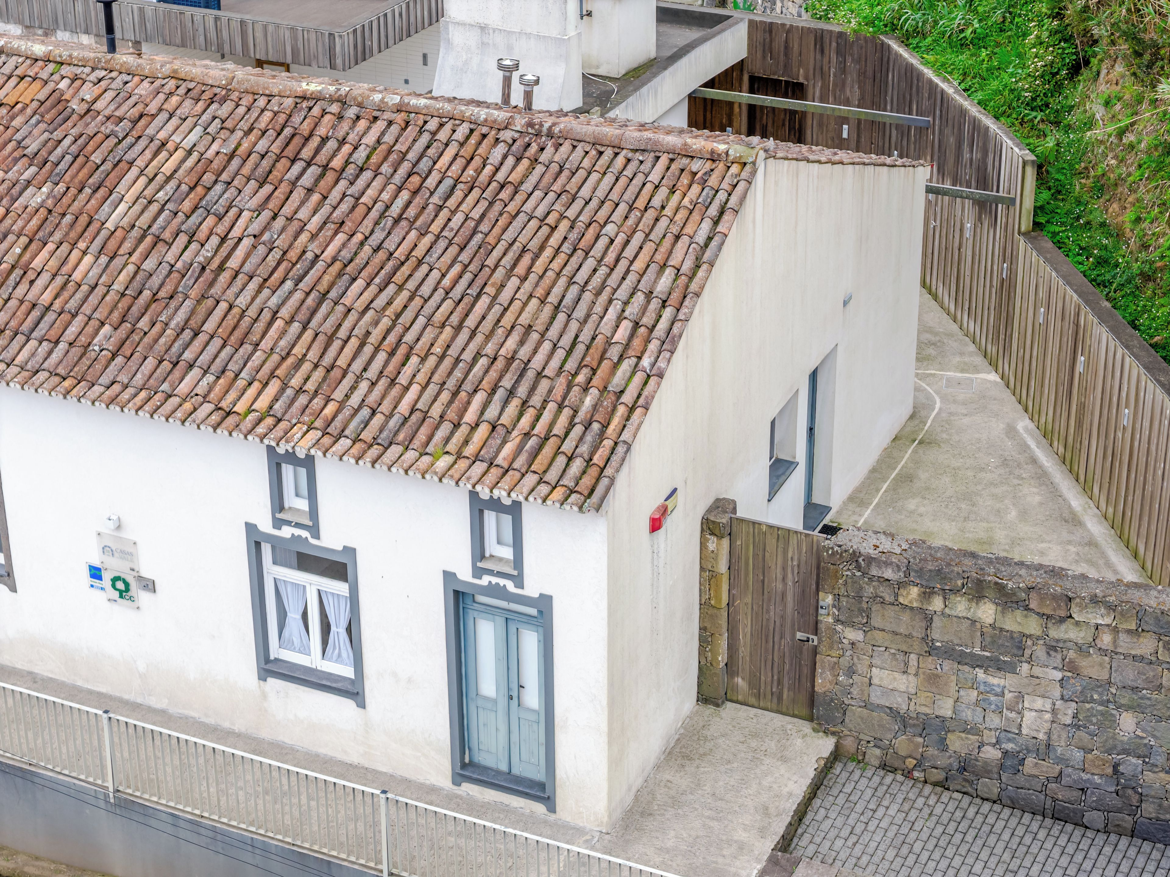 A building with a tiled roof, a small window with curtains, and a wooden gate.