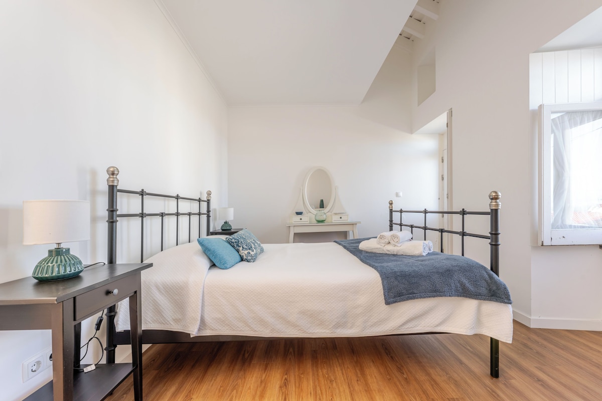 A bedroom with a bed, bedside table, lamp, and a window.
