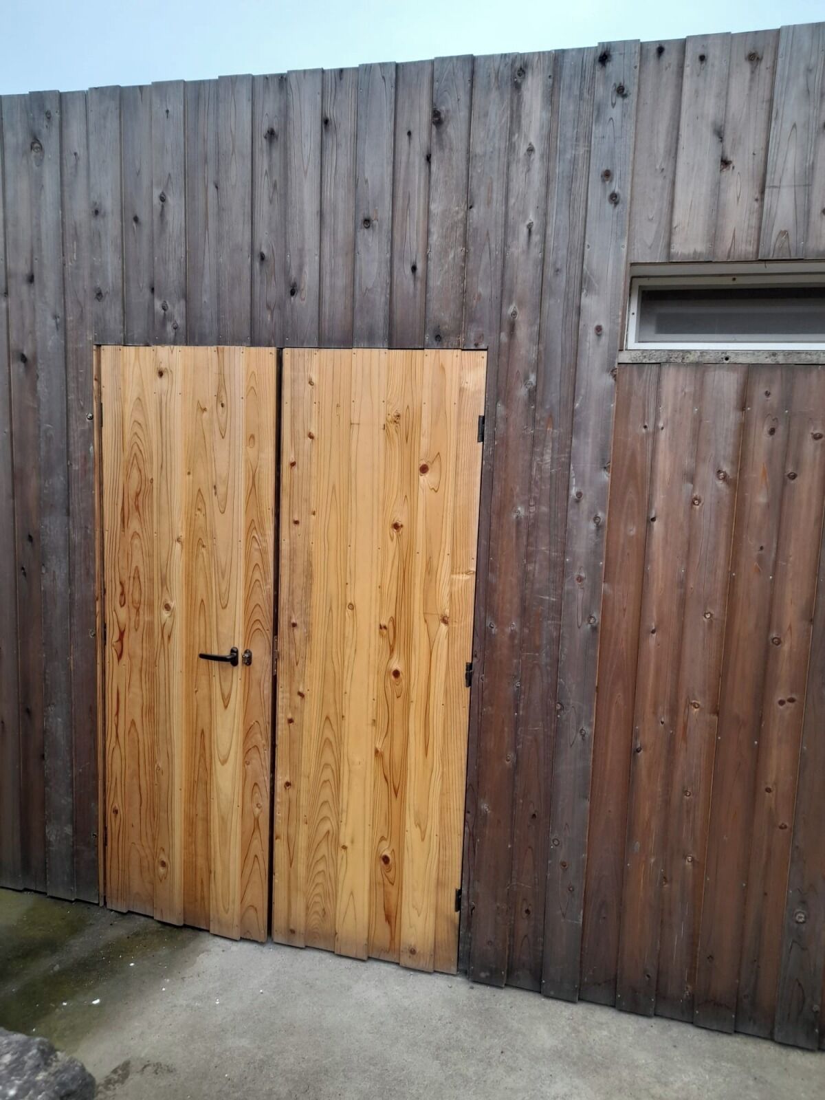 Cerca de madeira com porta dupla e uma pequena janela.