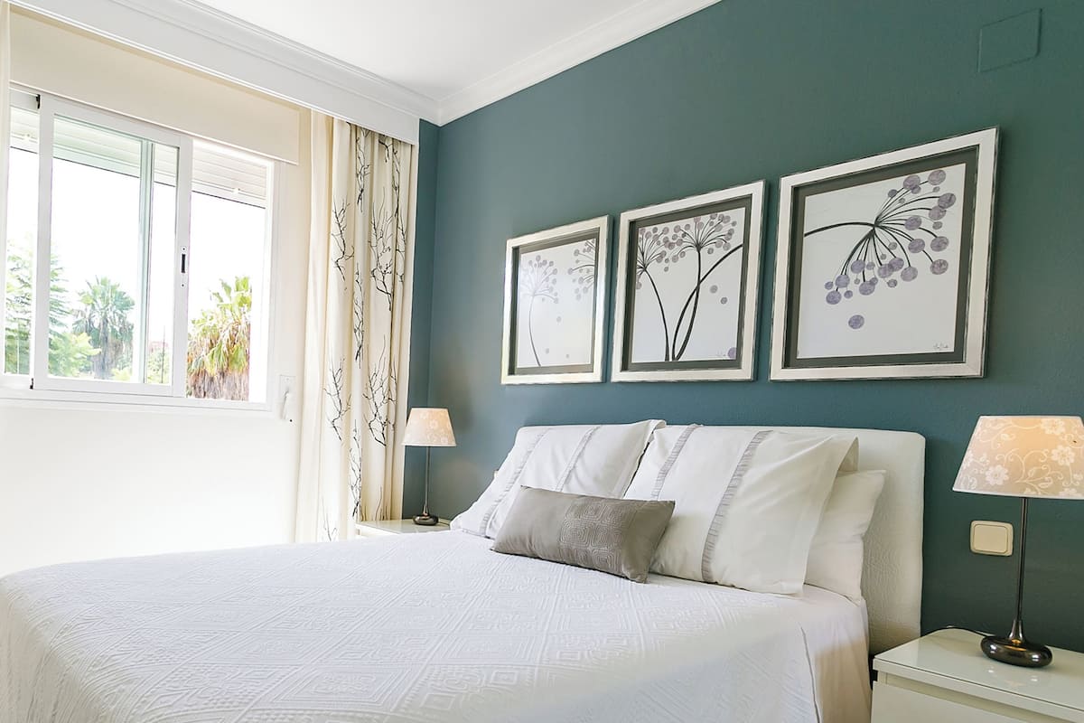 Un dormitorio con una cama grande, una mesita de noche, una lámpara y tres cuadros con motivos florales en la pared.