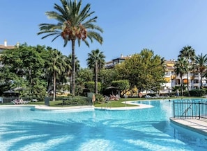 Una piscina envoltada de palmeres i un edifici amb balcons.