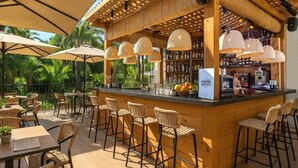 Een terras met een bar, rieten stoelen en tafels, een houten bar en hangende lampen.