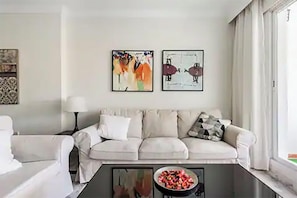 Un salon comprenant un canapé, une table basse avec un récipient, et deux œuvres d’art encadrées accrochées au mur.