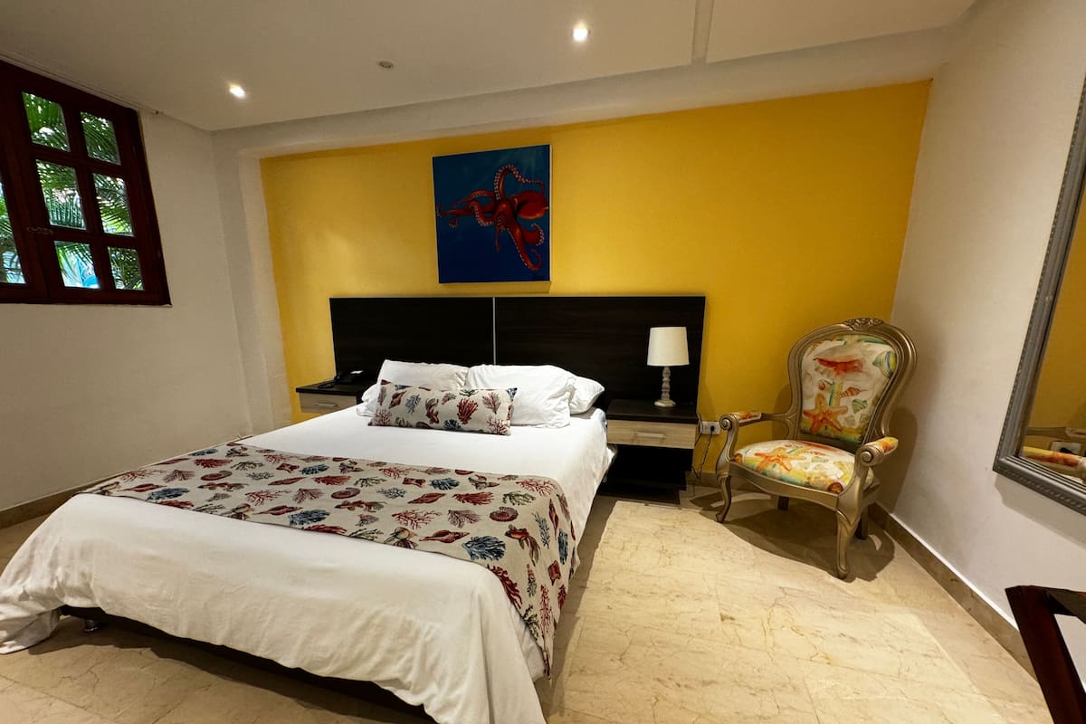 A hotel room with a large bed, a nightstand, a chair, and a painting on the wall.