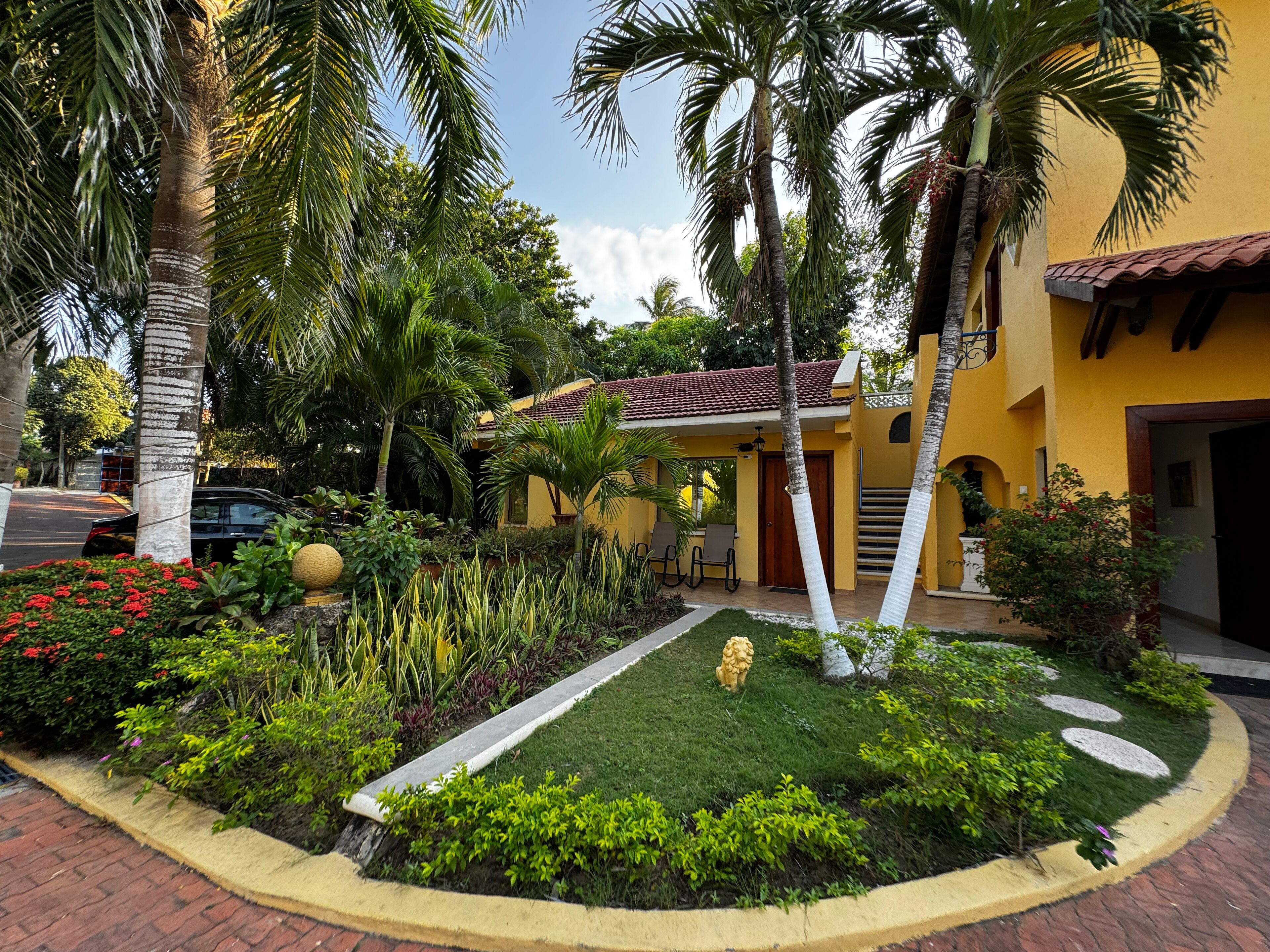A yellow building with a red-tiled roof, surrounded by lush greenery and palm trees.