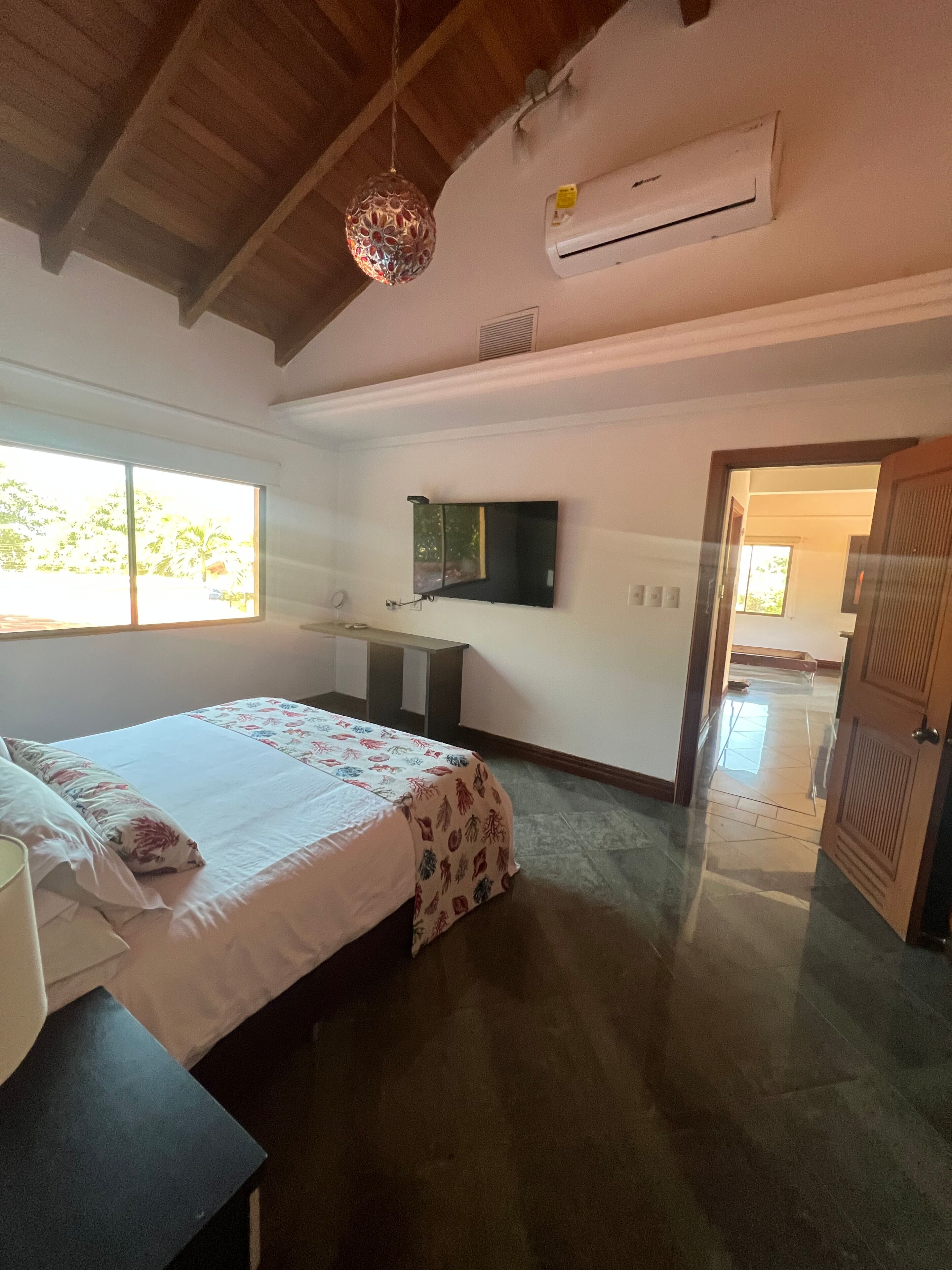 Un dormitorio con cama, mesita de noche y televisor montado en la pared.