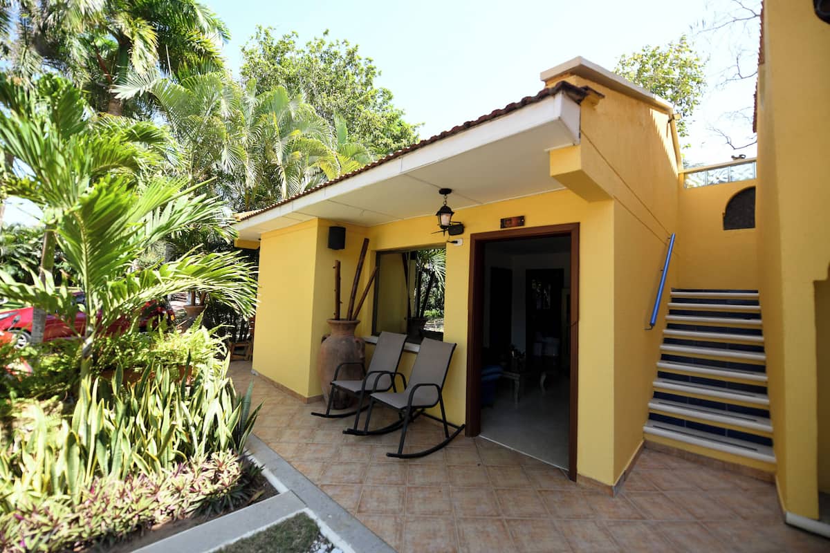 A yellow building with a covered patio area, a staircase, and a door leading inside.