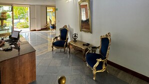 Un hall d’entrée spacieux avec un plafond haut, un escalier et un tableau représentant un paysage marin. On y trouve deux fauteuils décoratifs et un bureau avec un ordinateur portable.