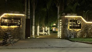 Vue nocturne de l’entrée du Porto Bello Hotel Boutique, avec ses enseignes illuminées et ses palmiers.