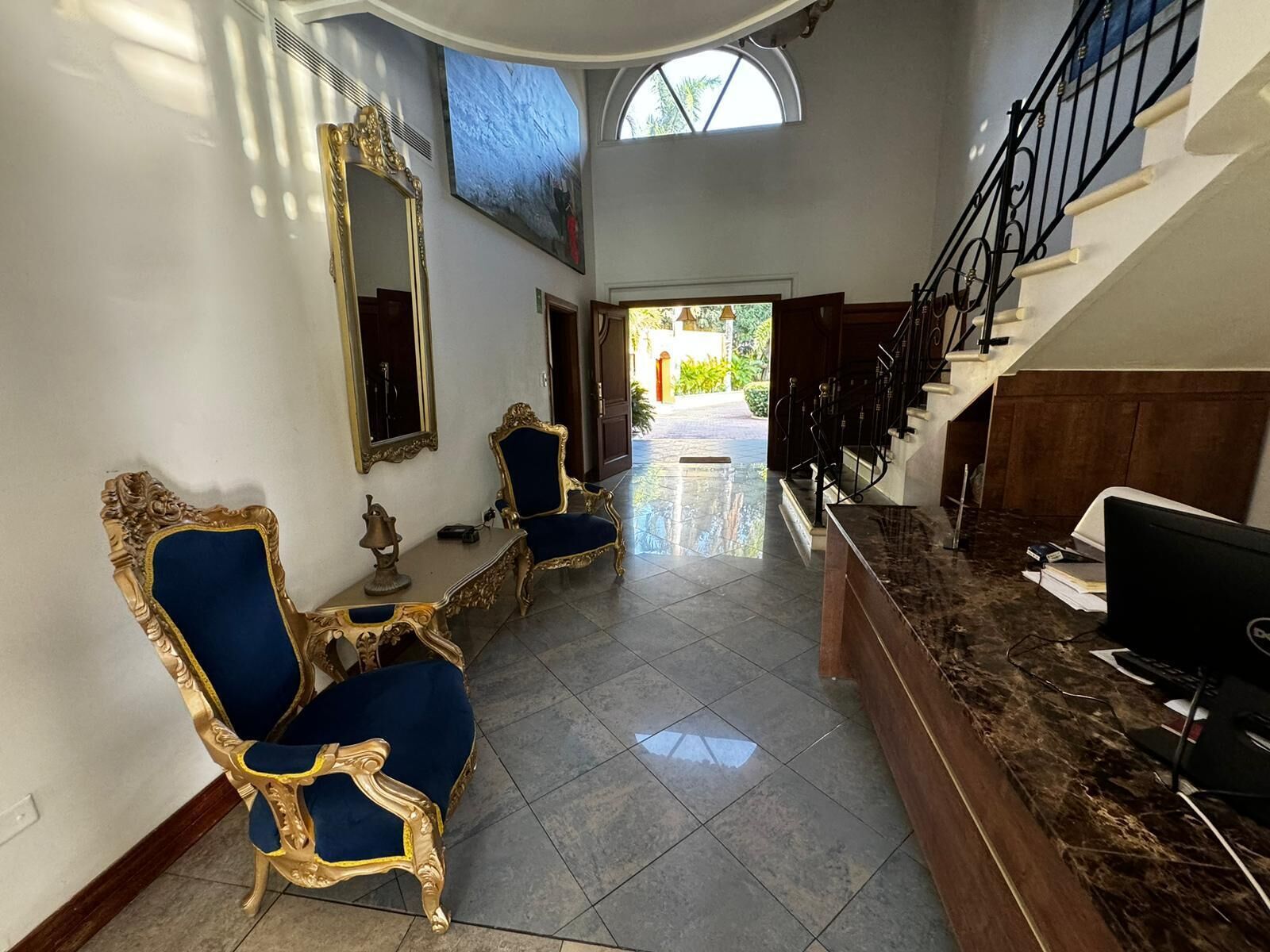 A spacious hallway with a marble floor, a grand staircase, and ornate gold-framed chairs.