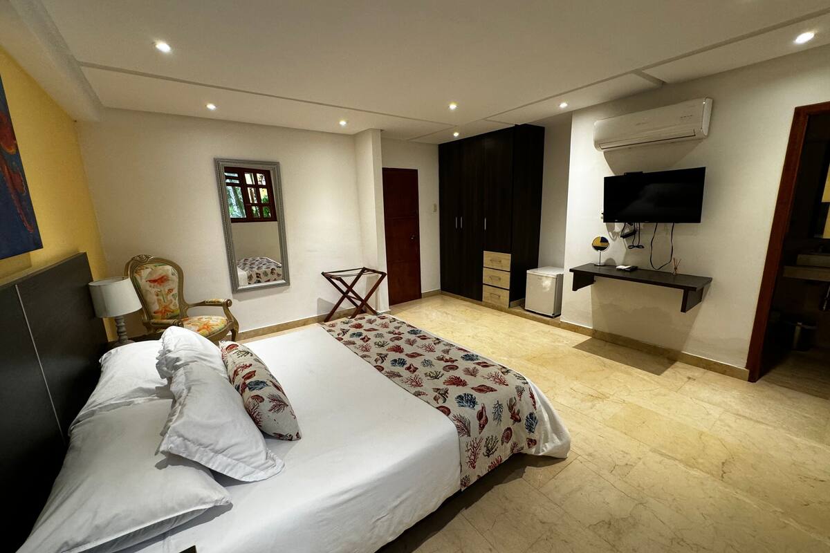 A hotel room with a bed, a desk, a chair, a TV, and a wardrobe.