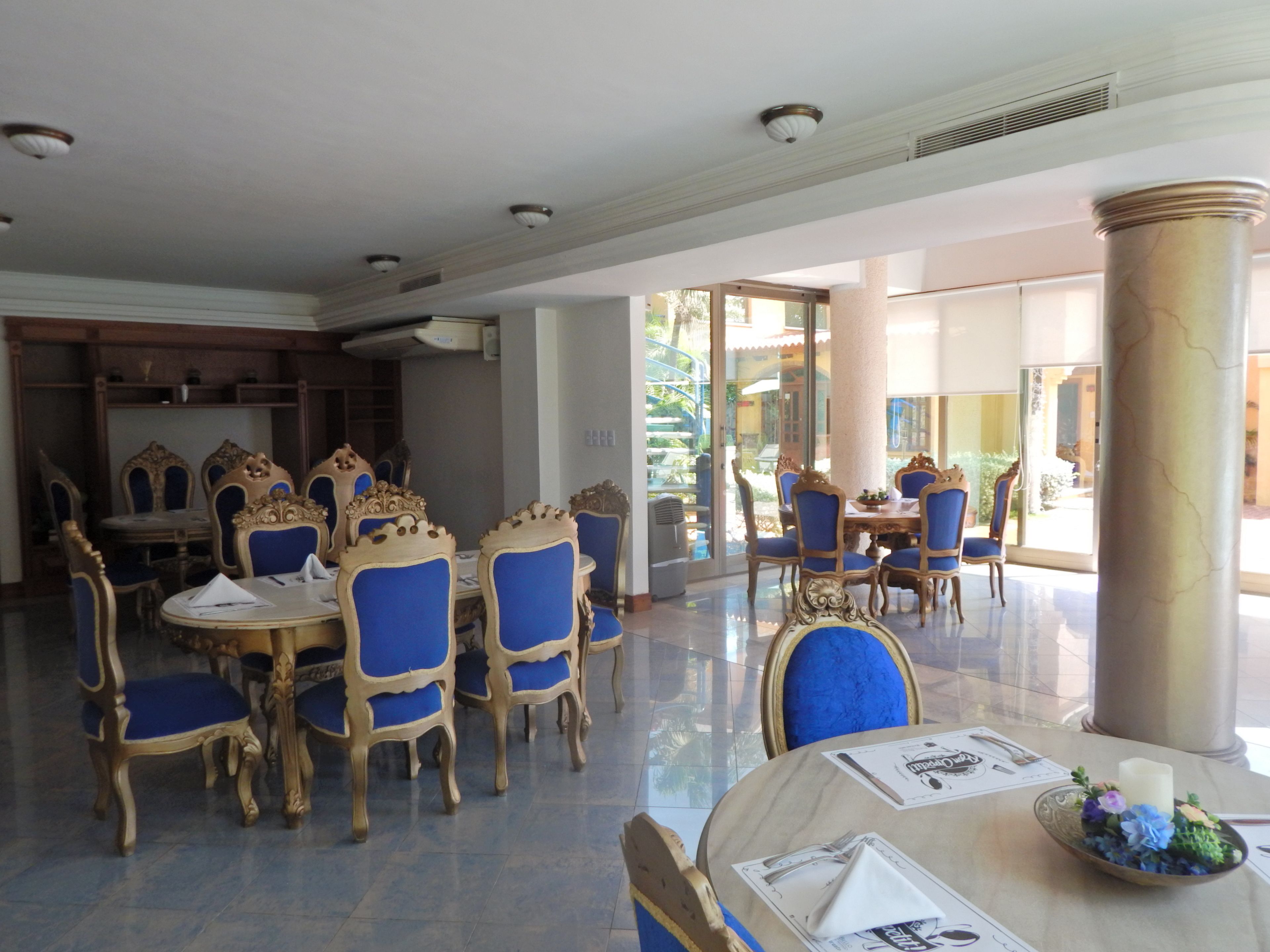 A dining area with ornate blue and gold chairs, a marble table, and a large pillar.