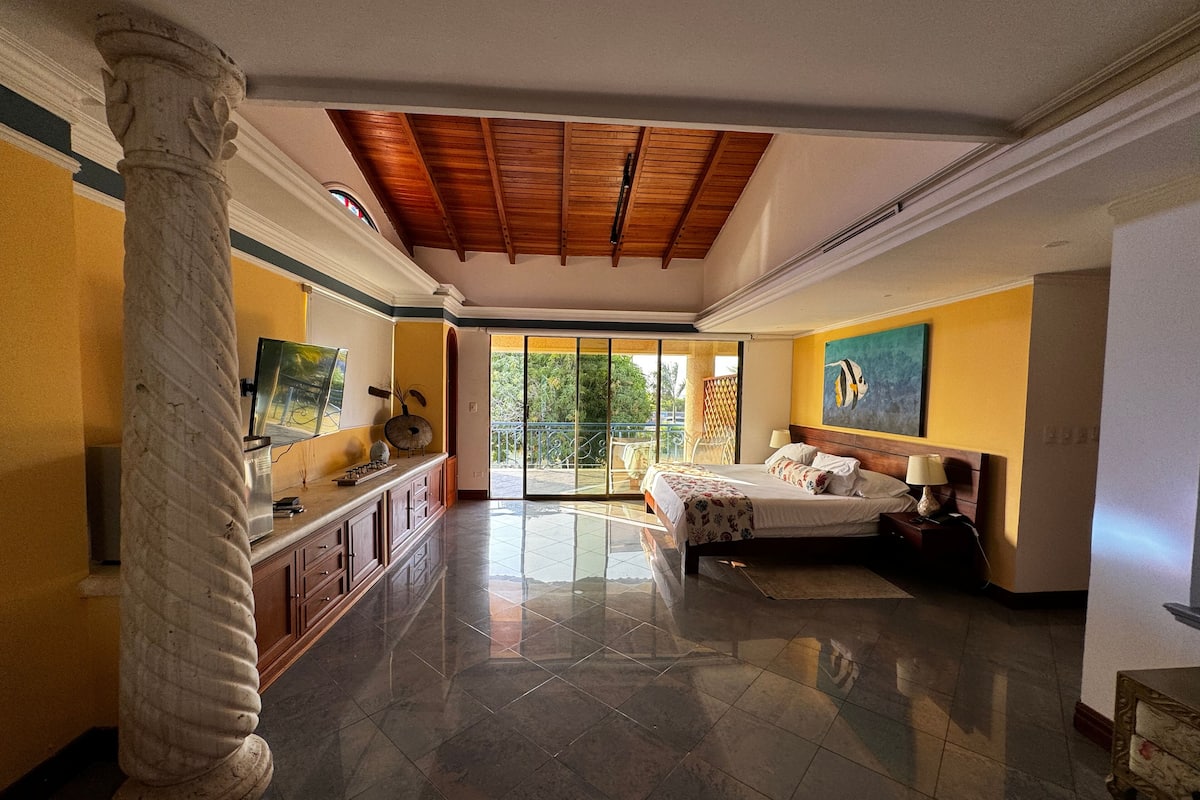 A spacious bedroom with a large bed, a balcony with a view, and a modern design.